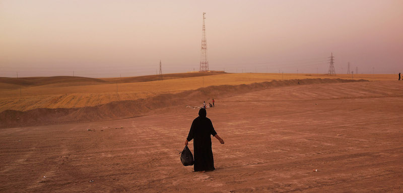 An Iraqi woman walks in a field beside a temporary displacement camp for Iraqis caught-up in the fighting in and around the city of Mosul on June 24, 2014 in Kalak, Iraq. Photo via Getty.